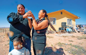 Gregory Harvey, his wife Iris and their daughter G'iada, 8, enjoy a playful splash of tap water for a portrait at their home near Round Rock, Arizona on Thursday. The family has recently been hooked up to running water after years of hauling water in jugs and water tanks, a task familiar to many throughout Navajo. Yet the expense and uncertainty of cleanliness with the water has brought a mixed blessing. "We're not drinking it yet," said Gregory Harvey. "Not until I get a good filter. And we will probably keep hauling water since we know the cost." &copy; 2011 Gallup Independent / Adron Gardner 